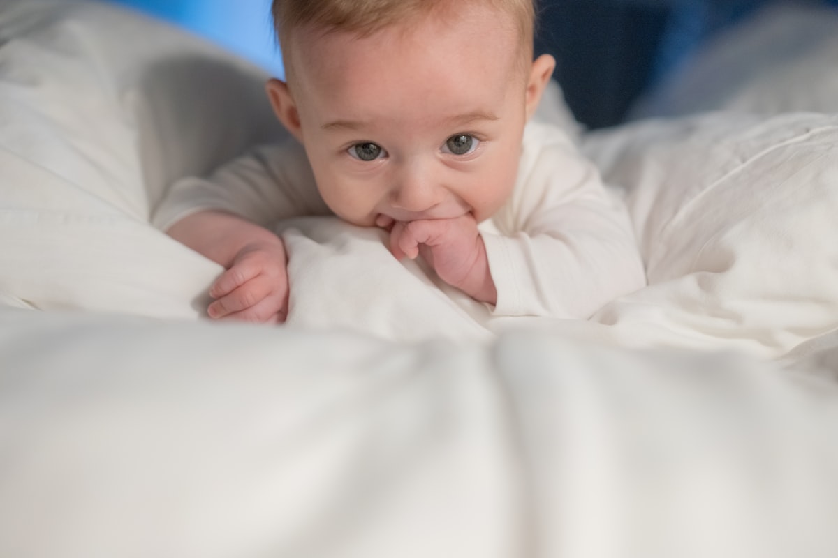 A baby laying on a bed with white sheets related to Design Your Own Dream Baby Bedding