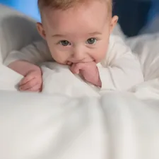 A baby laying on a bed with white sheets related to Design Your Own Dream Baby Bedding