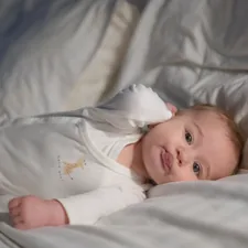 A baby laying on a bed with white sheets related to Gently Does It: Bringing the Forest to Your Little Buck