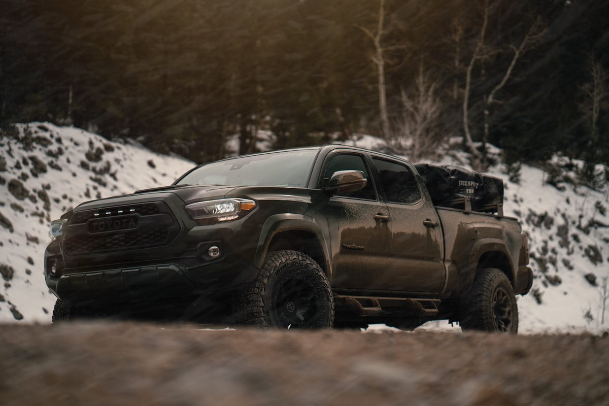a black truck driving on a dirt road with snow on the side related to Protecting Your Toyota Tacoma's Bed with a Custom Cover