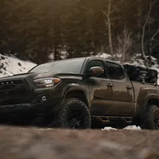 a black truck driving on a dirt road with snow on the side related to Protecting Your Toyota Tacoma's Bed with a Custom Cover