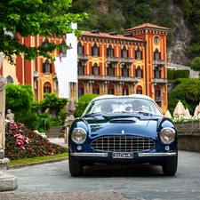 A blue car driving down a street next to a statue related to Embracing the Iconic Elegance of the Blue Rooster Chiminea