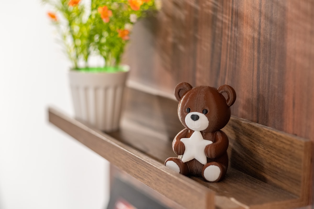 A brown 3D printed teddy bear by Snapmaker sits on a wooden shelf, holding a white star beside a flower pot. related to Charming Nursery Ideas with Cozy Bedding