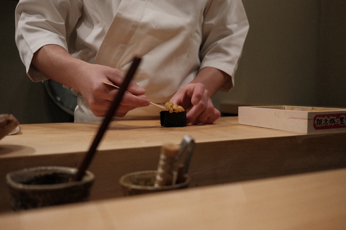 A chef prepares sushi on a wooden counter related to Master the Art of Sushi with a Sushi Making Kit from Bed Bath & Beyond