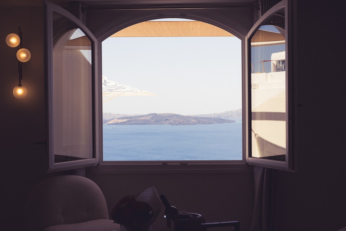 A cozy room with an open window offering a stunning view of the ocean and distant islands. The warm light fixtures on the wall add a comforting ambiance, while the clear blue sky and serene waters enhance the picturesque and relaxing scene. related to Elevate Your View: Window Valance Ideas for Large Windows