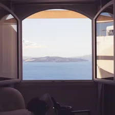 A cozy room with an open window offering a stunning view of the ocean and distant islands. The warm light fixtures on the wall add a comforting ambiance, while the clear blue sky and serene waters enhance the picturesque and relaxing scene. related to Elevate Your View: Window Valance Ideas for Large Windows