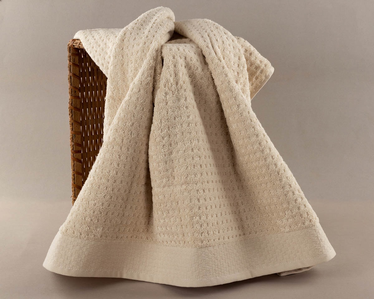 A cream-colored textured towel draped over a basket. related to Peacock Alley Matelasse Coverlet
