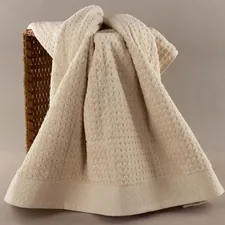 A cream-colored textured towel draped over a basket. related to Peacock Alley Matelasse Coverlet
