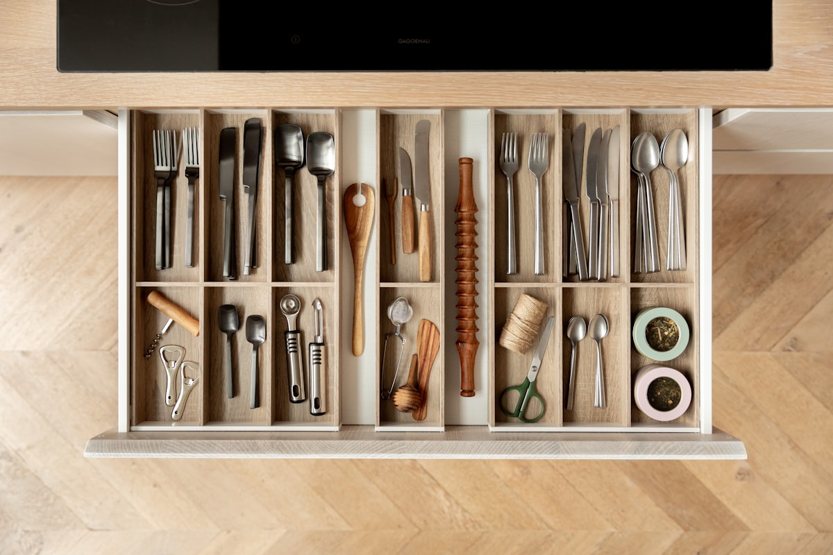 A cutlery drawer with wooden drawer inserts and black and silver cutlery. related to Maximizing Space: Innovative Storage Solutions for Small Entryways
