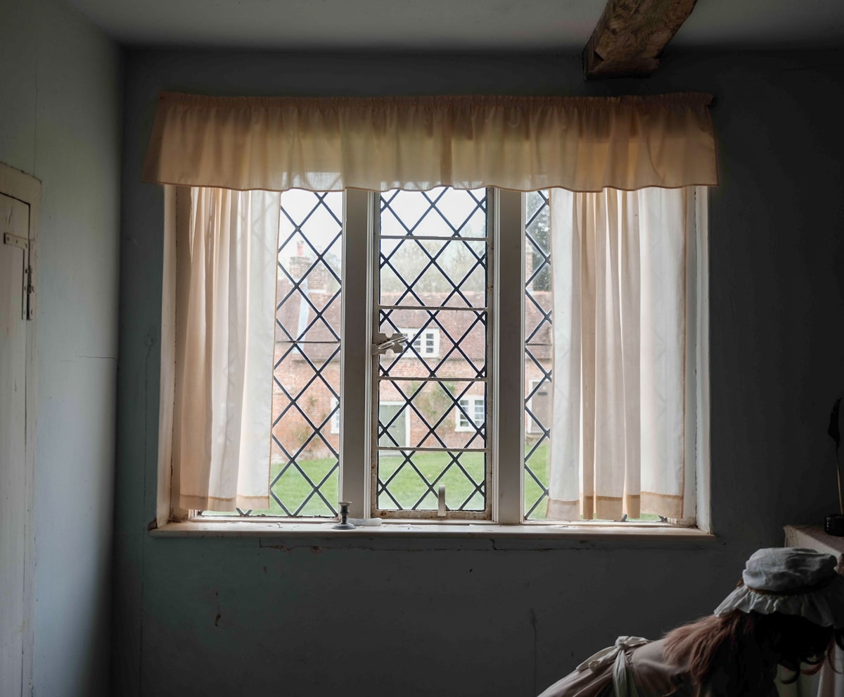 A diamond-paned window with sheer curtains overlooks a garden. related to 3 Inch Rod Pocket Valance: A Comprehensive Guide