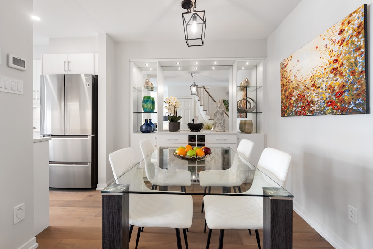a dining room table with white chairs and a painting on the wall related to Elevate Your Dining Experience: Glass Sideboards for the Perfect Room