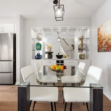 a dining room table with white chairs and a painting on the wall related to Elevate Your Dining Experience: Glass Sideboards for the Perfect Room