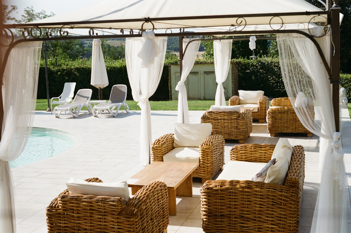 A draped pergola with wicker sofas overlooks a sunlit pool at an Italian countryside villa. related to How to Decorate a Canopy Bed