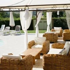 A draped pergola with wicker sofas overlooks a sunlit pool at an Italian countryside villa. related to How to Decorate a Canopy Bed