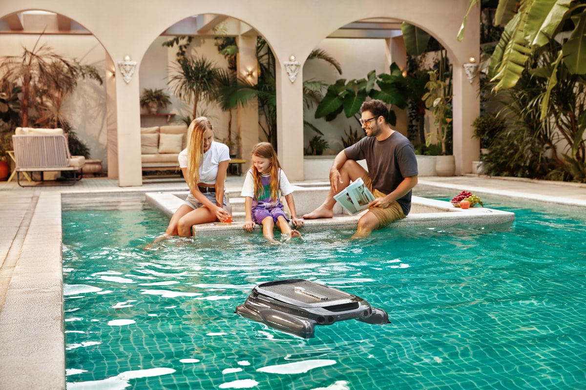 A family relaxing poolside as Aiper Surfer S1 pool skimmer glides through the water. related to Discover the Comfort and Convenience of the Peapod Plus Travel Bed