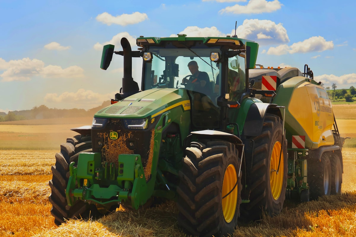 A green tractor with a baler working in a field. related to Transform Your Child's Room with a Tractor Bedding Set