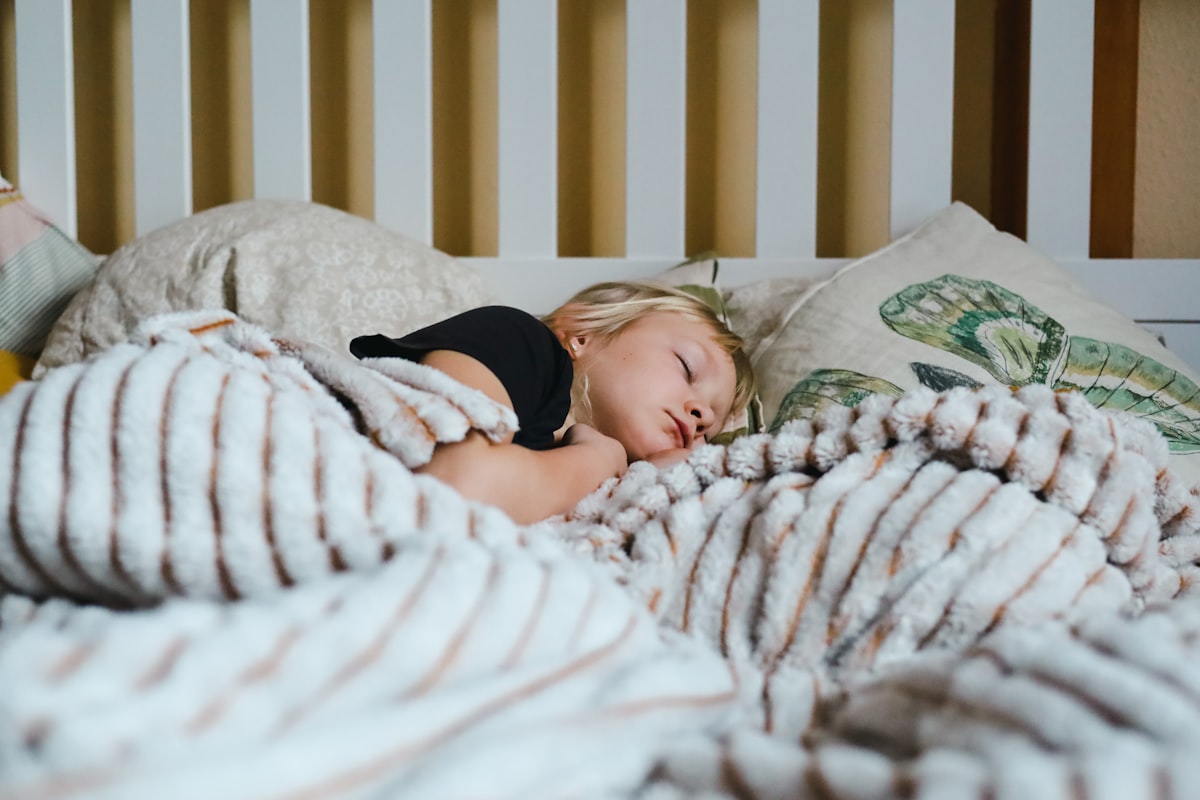 a little girl sleeping in a bed with a blanket related to The Ultimate Guide to Choosing the Right Toddler Bed Rails