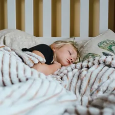 a little girl sleeping in a bed with a blanket related to The Ultimate Guide to Choosing the Right Toddler Bed Rails
