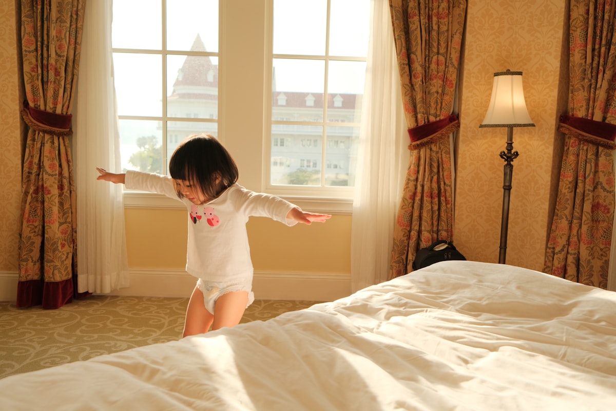 A little girl standing on a bed in a bedroom related to Snuggle Up & Stay Safe: Protecting Your Child With Bed Rails