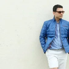 a man in a blue jacket leaning against a white wall related to Experience Luxury with our Quilted Coverlet Hotel Collection