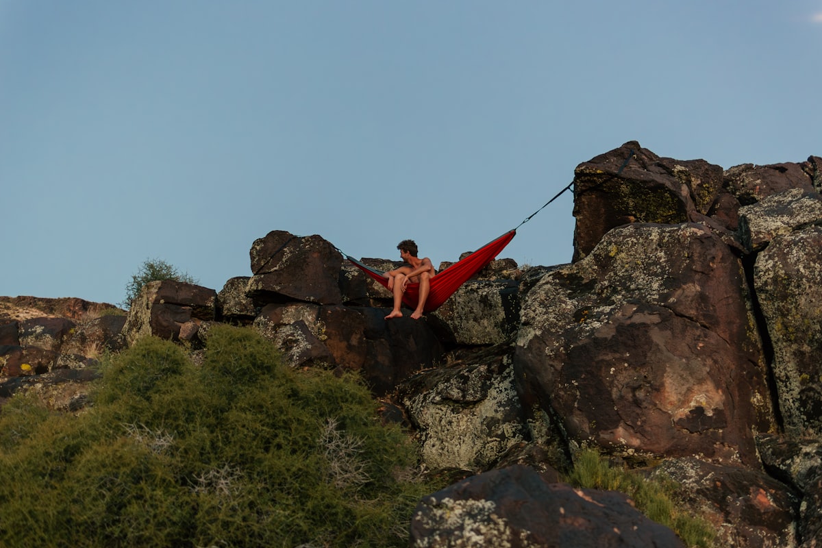 a man sitting on top of a large rock related to Elevate Your Outdoor Experience with a Hanging Bed