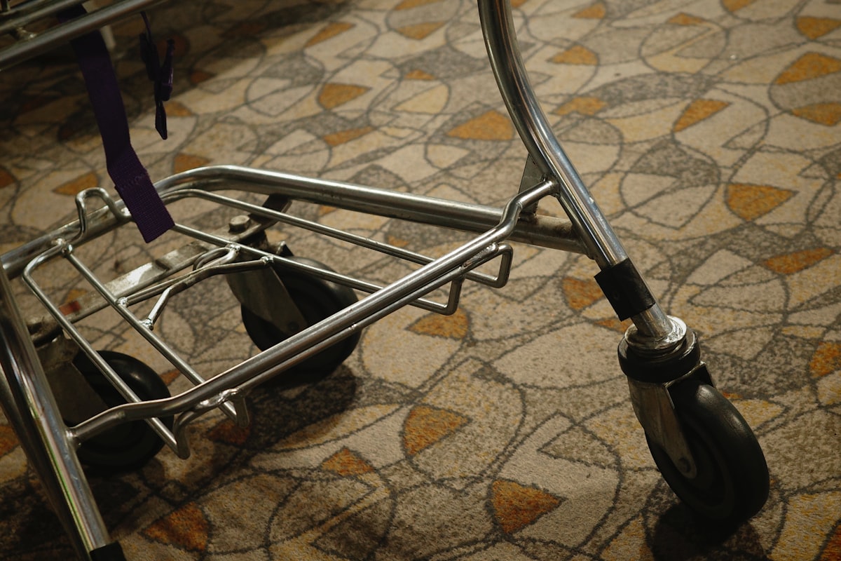 A metal luggage cart sits on patterned carpet. related to Elevate Your Space with Bed Risers for Wheels: A Game-Changer for Your Home
