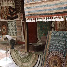 A person arranging patterned rugs in a shop filled with hanging textiles related to Explore Stylish Rugs for Every Home