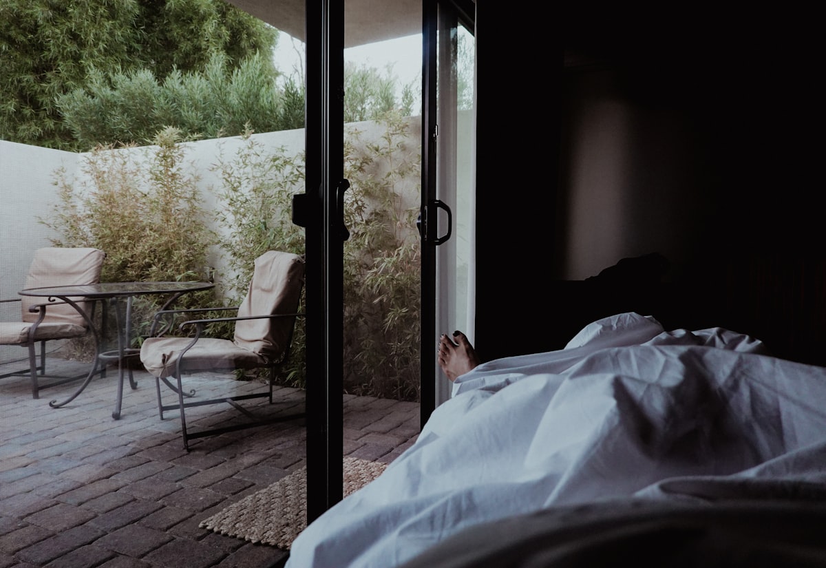 a person laying in a bed next to a sliding glass door related to Elevate Your Slumber: Luxury Bed Coverlets for the Modern Home