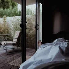a person laying in a bed next to a sliding glass door related to Elevate Your Slumber: Luxury Bed Coverlets for the Modern Home
