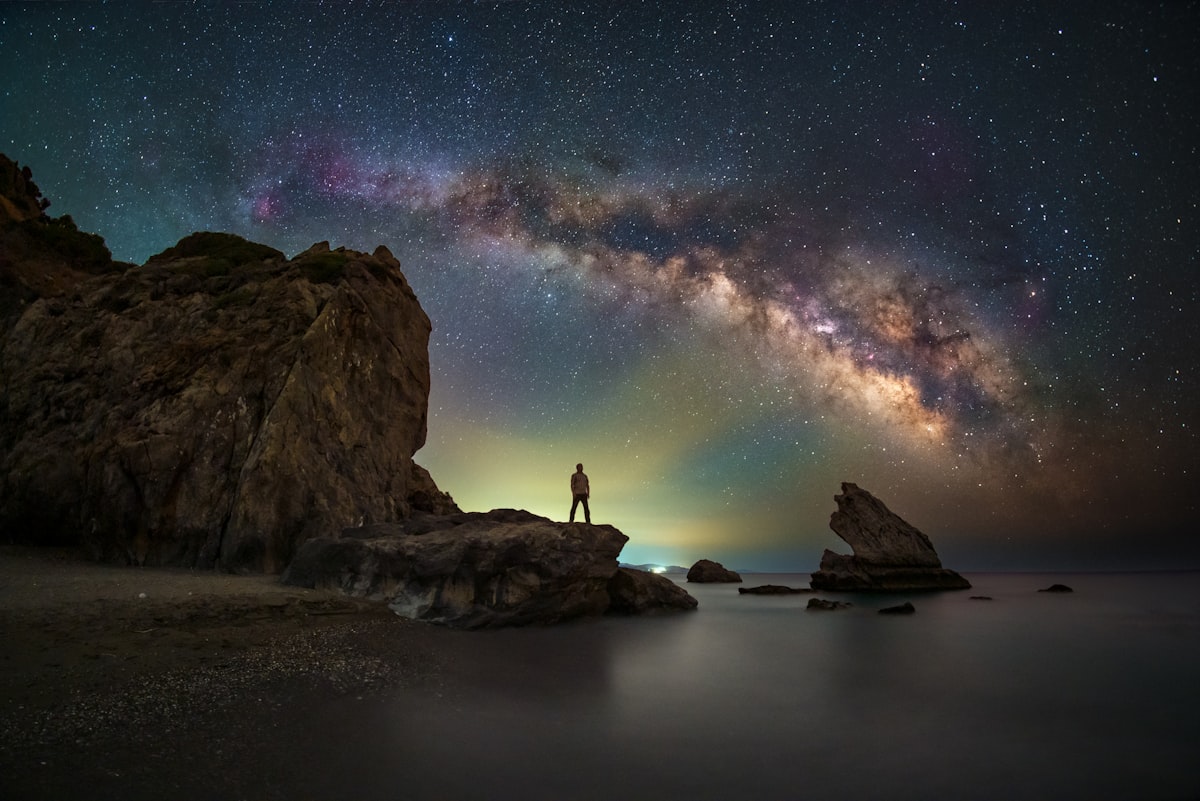 A person standing on a rock looking at the stars related to Exploring the Cosmic Dreams: Galaxy Bed Spread
