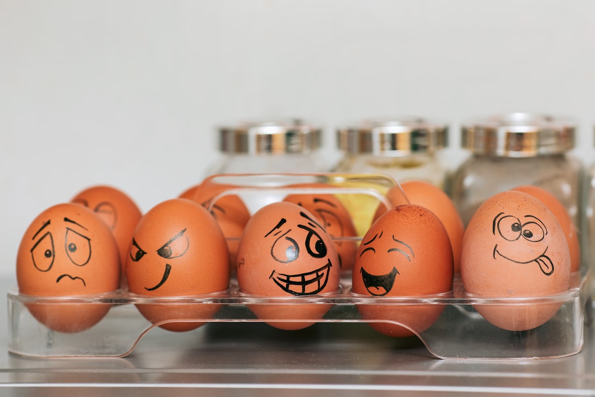 A photograph (wallpaper, picture) of eggs with different emotions against a background of blurred spices and a smooth gray wall.  Whole painted eggs in the kitchen, expressing a spectrum of emotions from sadness to joy or madness. Eggs with smile and crazy face. related to How Many Eggs Do Bed Bugs Lay?
