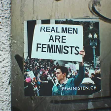 a picture of a man holding a sign that says real men are feminists related to What Men Really Want in Bed, Revealed: Behind the Scenes of Their Mental and Emotional Needs