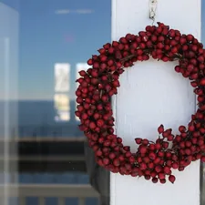 a red berry wreath hangs on a white door related to Deck the Entryway: Creative and Festive Christmas Decor Ideas