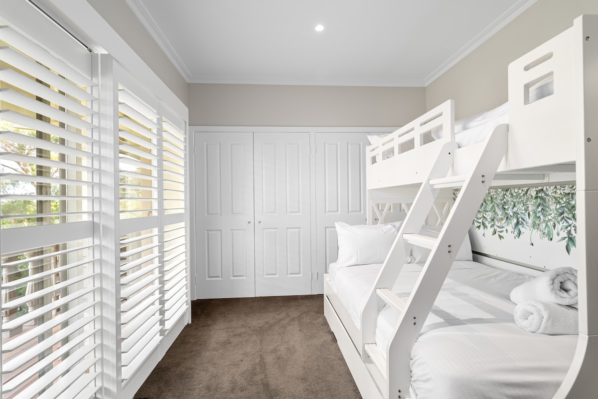 A room with bunk beds and white shutters related to Maximizing Space with Style: The Ultimate Guide to Triple Bunk Beds