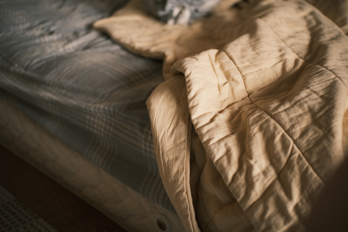 A rumpled bed with a beige comforter and striped sheets. related to Bedspread vs. Coverlet: What's the Difference?