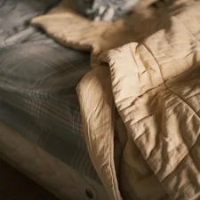 A rumpled bed with a beige comforter and striped sheets. related to Bedspread vs. Coverlet: What's the Difference?