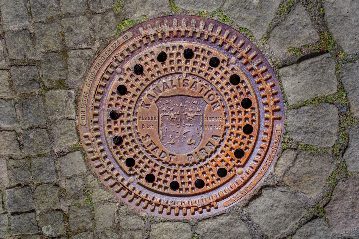 A rusty manhole cover is in the pavement. related to Embark on a Cast Iron Chiminea Burning Bonfire Experience