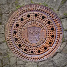 A rusty manhole cover is in the pavement. related to Embark on a Cast Iron Chiminea Burning Bonfire Experience