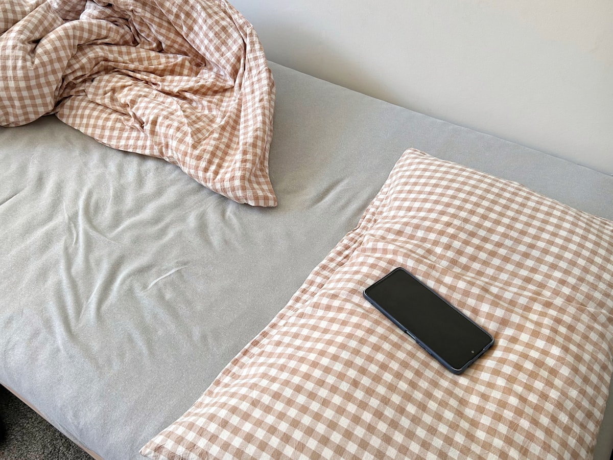 A smartphone rests on a checkered pillow on a bed. related to Single Bed Coverlets