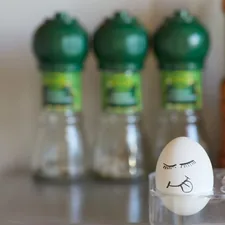 A smiling face with eyes, mouth, and tongue hanging out is drawn on a chicken egg. Emotional egg in the background of the kitchen related to Big Green Egg Chiminea Price