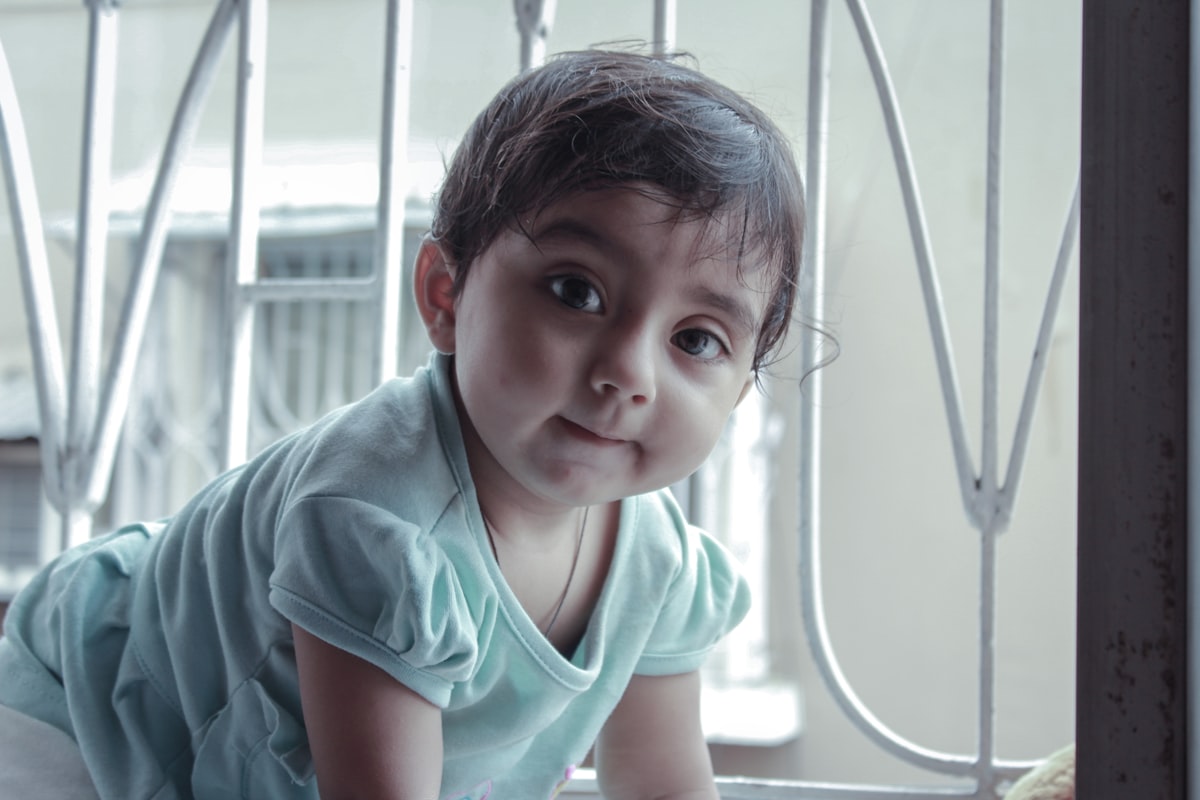 A soulful close-up of a baby girl with big curious eyes, softly biting her lip as she gazes into the camera. Dressed in mint green and surrounded by gentle light from a nearby window, this candid captures the quiet wonder and innocence of childhood perfectly. related to Protecting Your Little One: The Importance of Baby Bed Guards