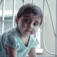 A soulful close-up of a baby girl with big curious eyes, softly biting her lip as she gazes into the camera. Dressed in mint green and surrounded by gentle light from a nearby window, this candid captures the quiet wonder and innocence of childhood perfectly. related to Protecting Your Little One: The Importance of Baby Bed Guards