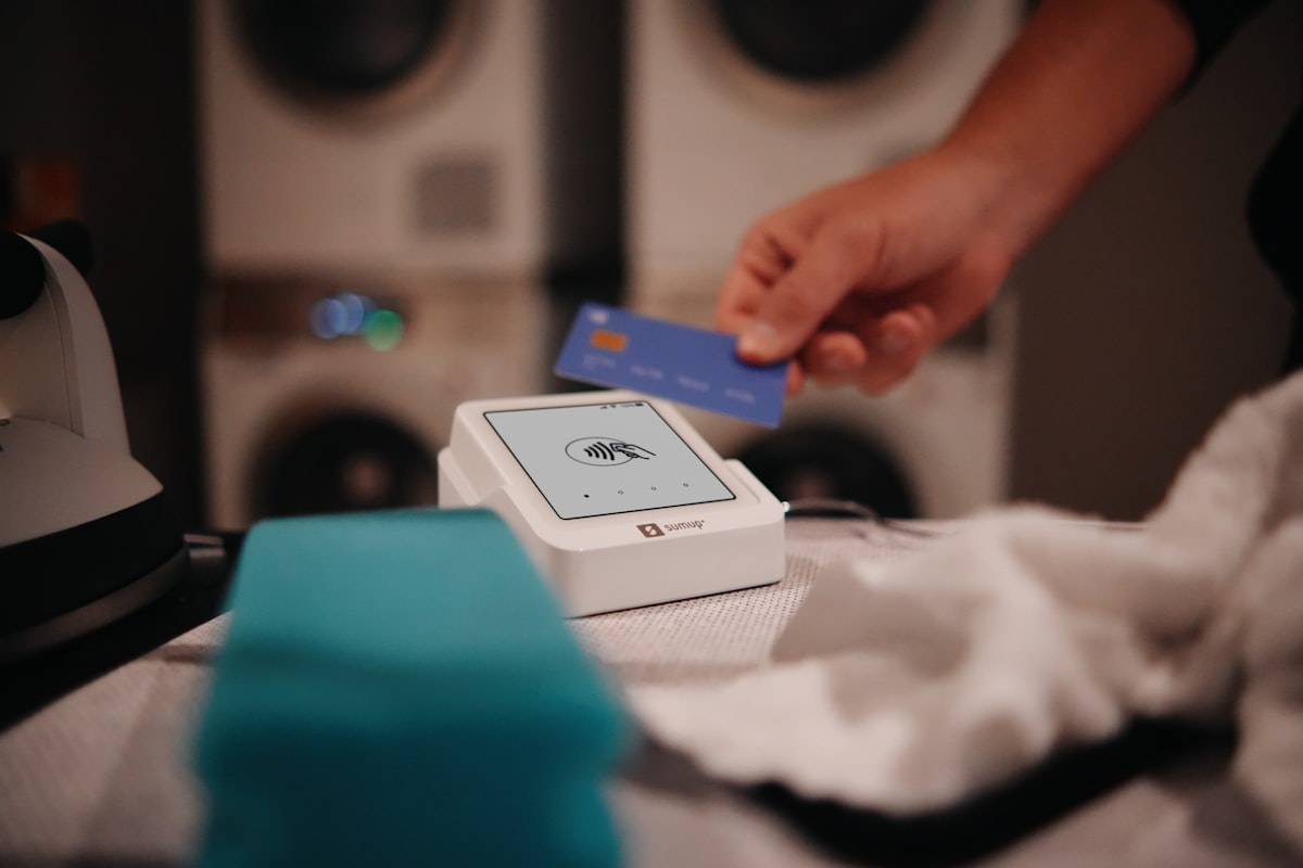 A SumUp Solo card reader placed next to folded towels in a laundry service environment, showing how small businesses can offer seamless point of sale transactions with cashless payments. related to Know Your Bed Bath & Beyond Gift Card Balance