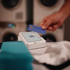 A SumUp Solo card reader placed next to folded towels in a laundry service environment, showing how small businesses can offer seamless point of sale transactions with cashless payments. related to Know Your Bed Bath & Beyond Gift Card Balance