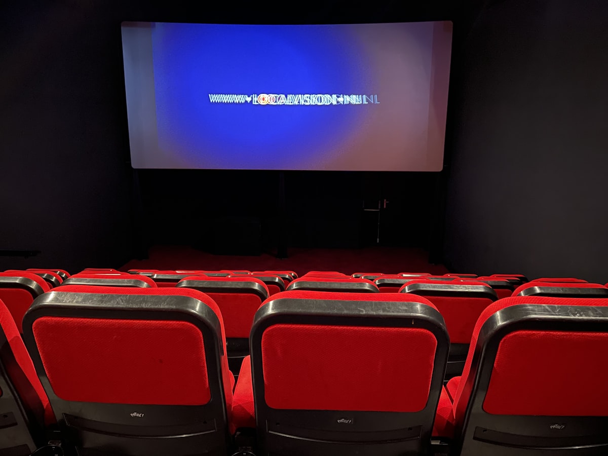 a theater with red seats and a projector screen related to Revolutionizing Comfort: The Rise of Movie Theatres with Beds