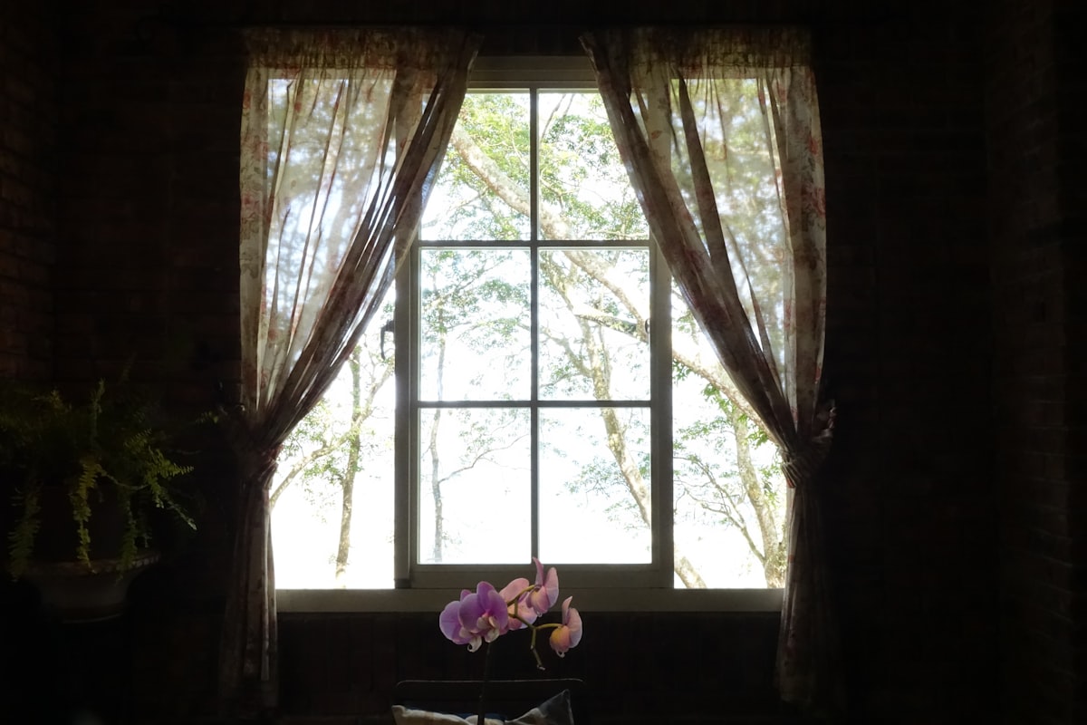 a window with curtains and a vase with flowers in it related to The Art of Window Dressing: Valances and Swags