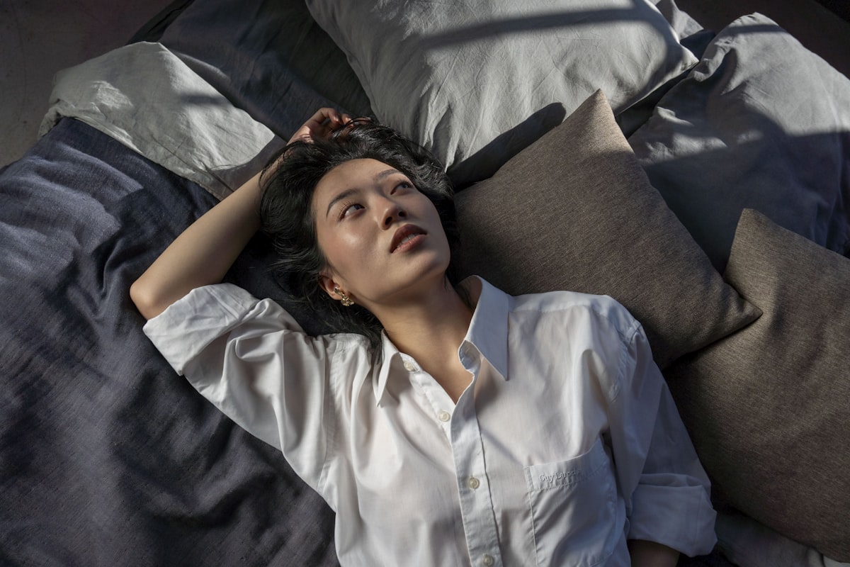 A woman in a white shirt lies on a bed. related to Sleep in Harmony: The Bliss of Reverie Adjustable Beds