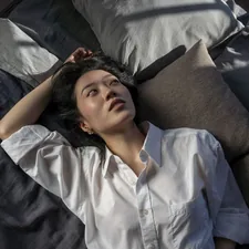 A woman in a white shirt lies on a bed. related to Sleep in Harmony: The Bliss of Reverie Adjustable Beds