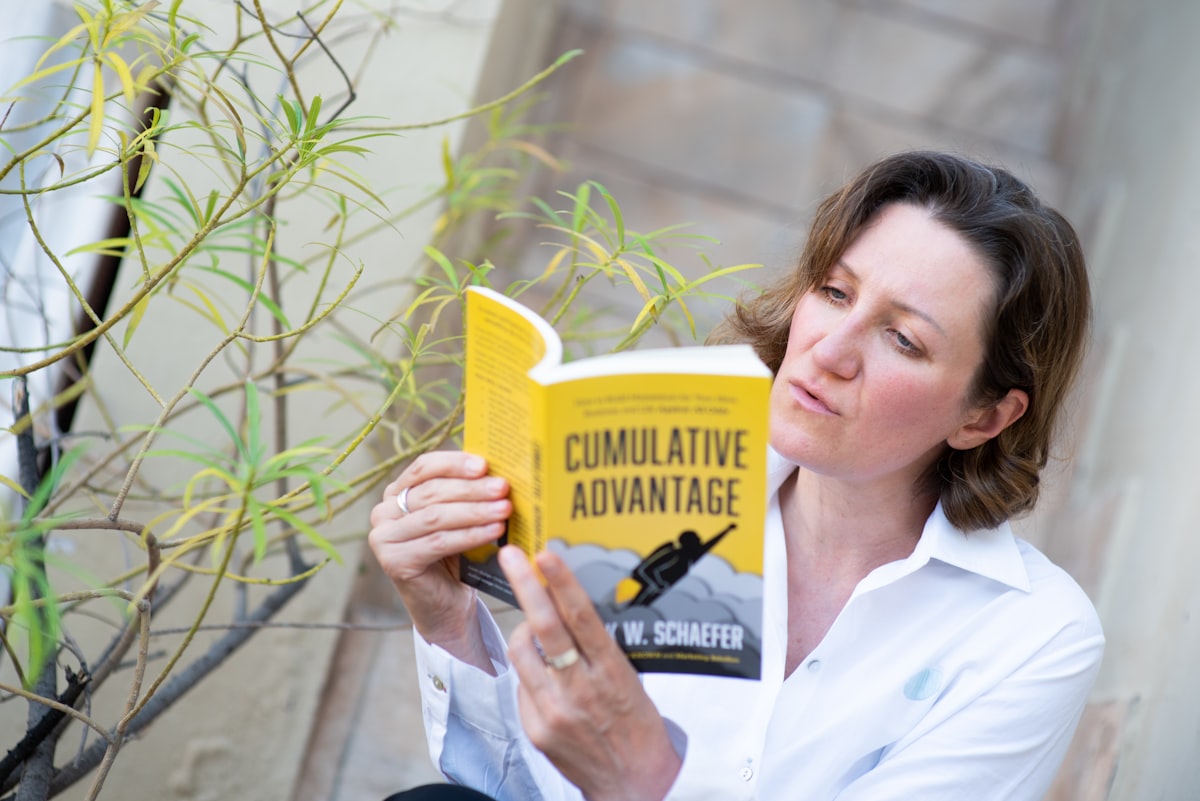 A woman in white shirt, sitting on the steps outside, reading a yellow paperback book related to Martha Stewart Coverlets: A Comprehensive Guide