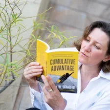 A woman in white shirt, sitting on the steps outside, reading a yellow paperback book related to Martha Stewart Coverlets: A Comprehensive Guide
